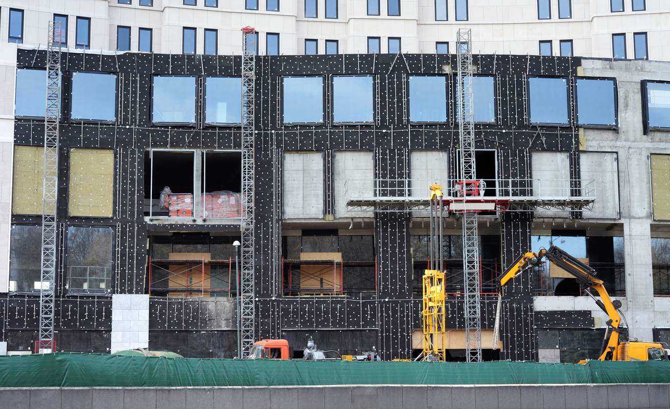 Façade d'un immeuble de bureaux en cours d'isolation par l'extérieur, panneaux isolants chevillés et échafaudage de levage