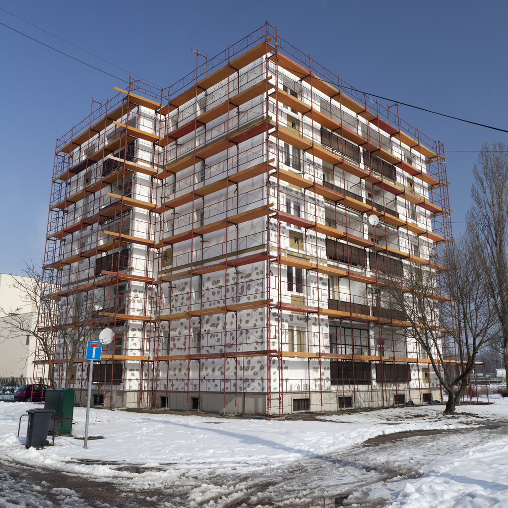 Bâtiment sous échafaudage complet, façades recouvertes de panneaux isolants collés par plots, en période hivernale
