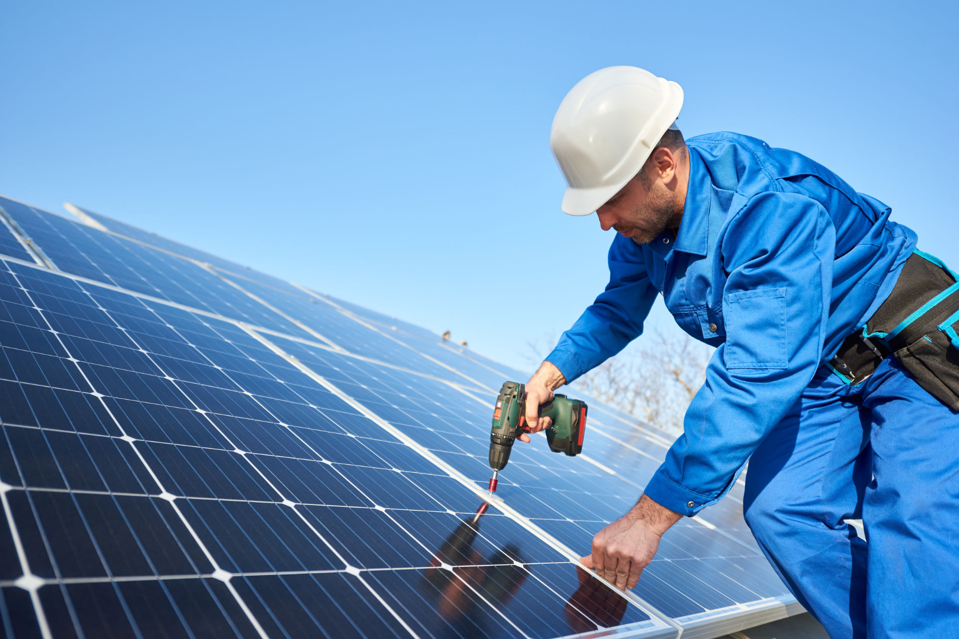 Technicien casqué vissant la fixation d'un module photovoltaïque sur une toiture