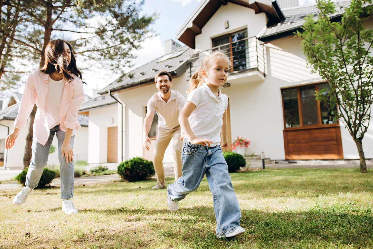 Famille jouant dans le jardin devant une maison individuelle rénovée et isolée par l'extérieur