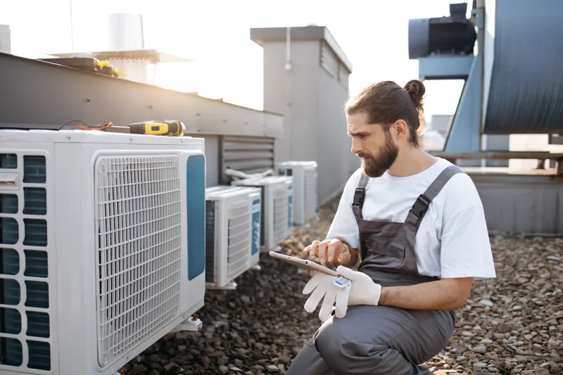 Technicien contrôlant les groupes extérieurs en toiture — climatisation réversible immeuble d’habitation dans le Grand Est